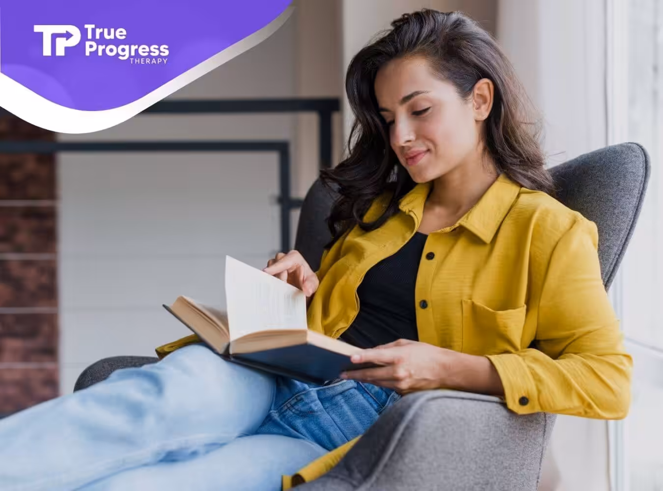 A female BCBA relaxing in a chair while reading a book near a bright window after an ABA therapy session.