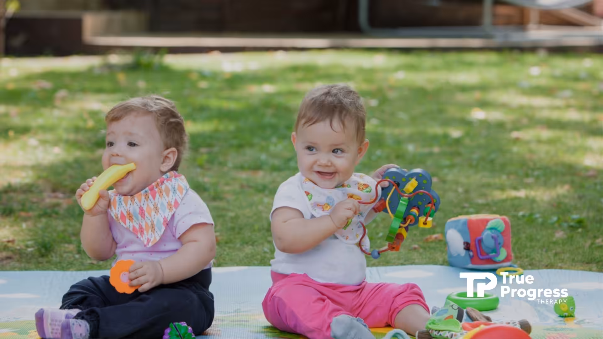 Two babies sitting on a mat with toys, engaging in sensory play for developmental growth.