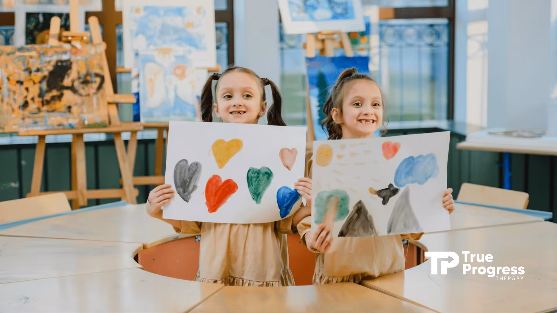 Two autistic girls smiling while holding paintings with hearts during ABA therapy in New Jersey.