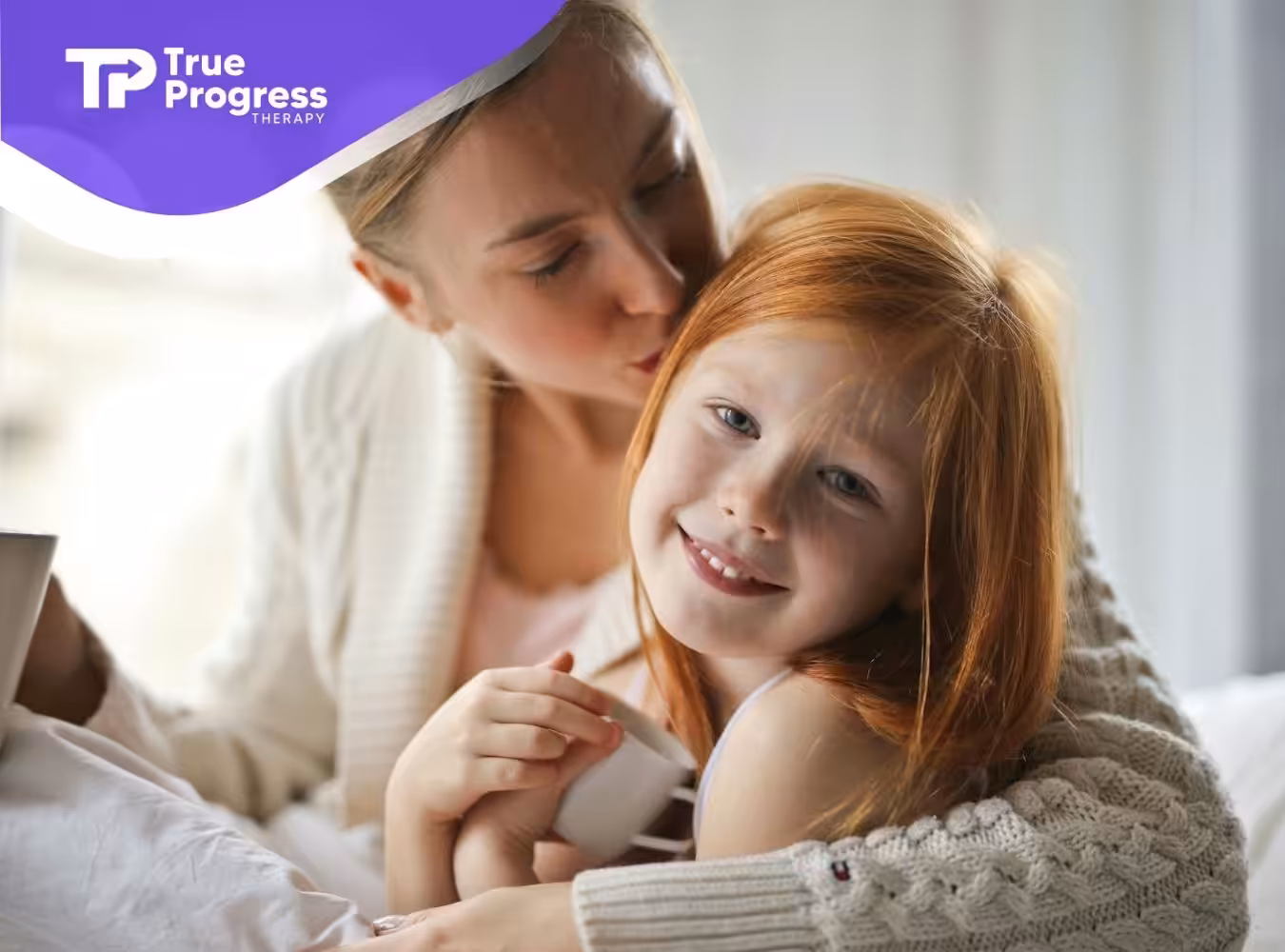 Smiling autistic girl hugged by mother who kisses her on the head during in-home ABA therapy in NJ.