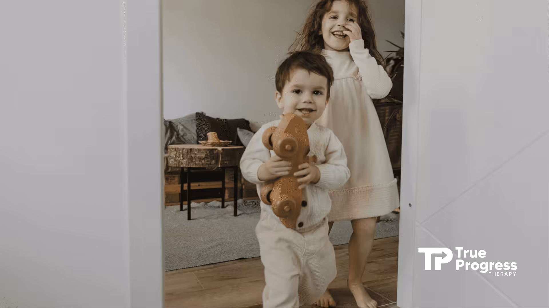 An autistic boy holding a wooden toy car and smiling with a girl behind him at a living room in NJ.