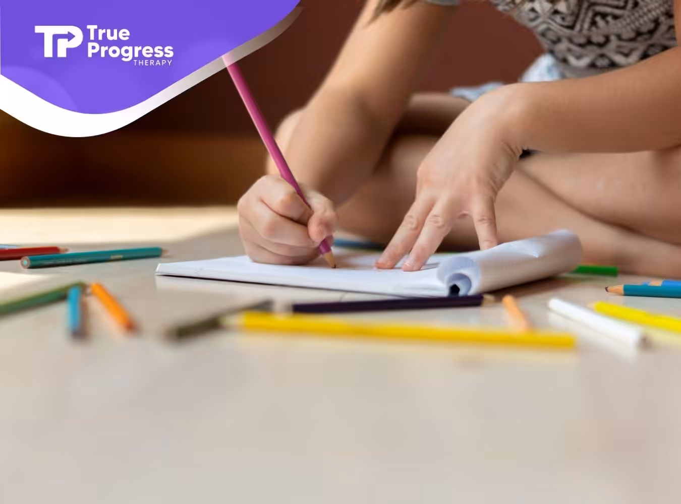 An autistic child drawing with colorful pencils on a notepad on the floor at home in New Jersey.