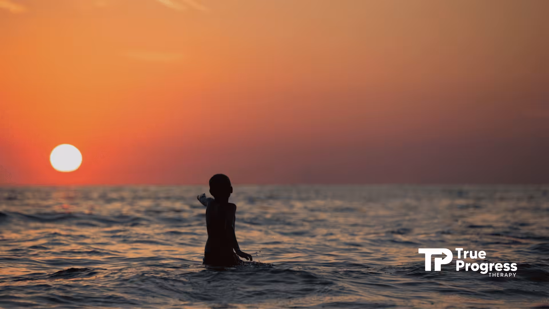 Autistic child standing in ocean water during sunset, reaching toward the setting sun in New Jersey.