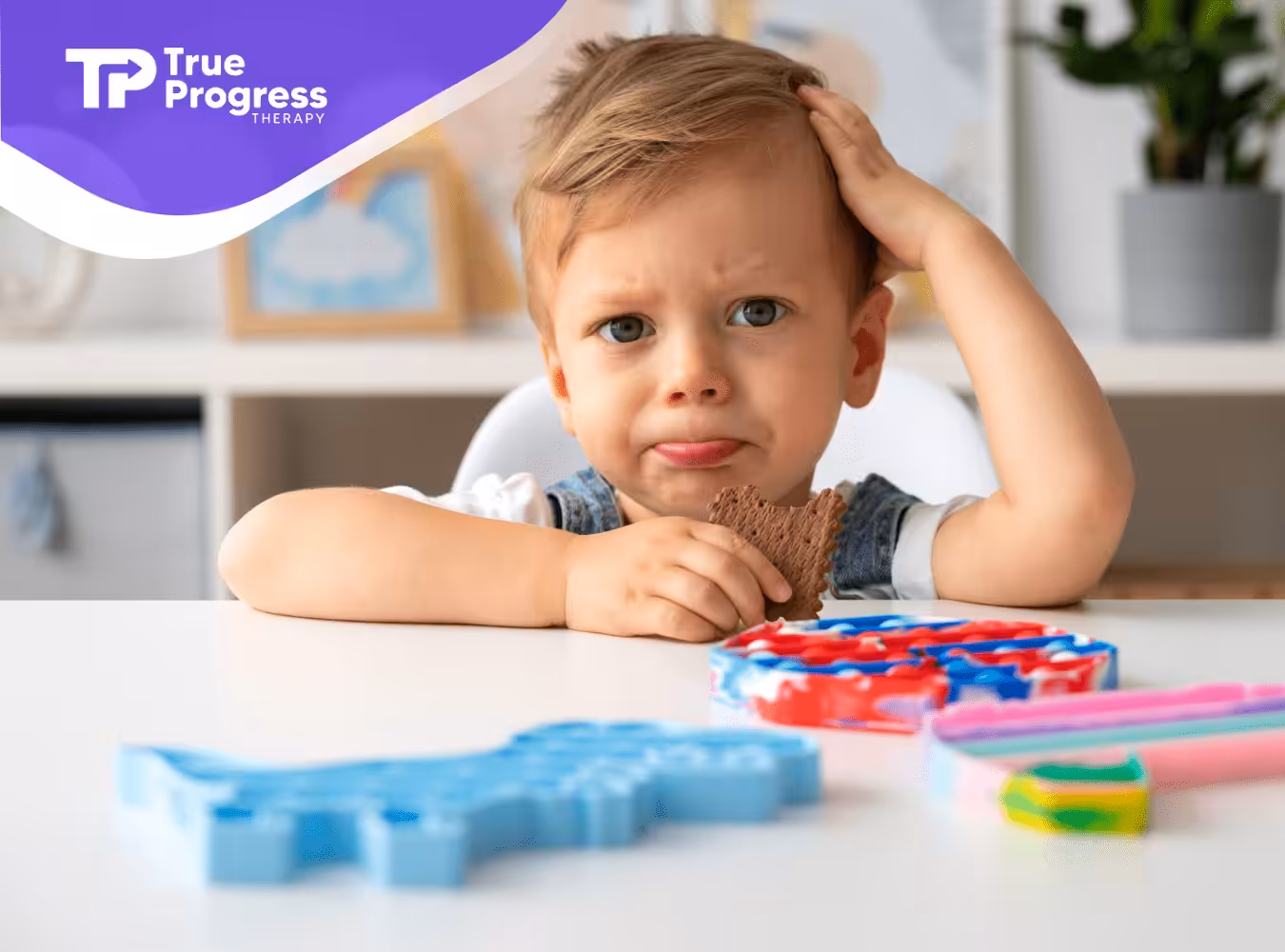 A kid sitting on a table holding a biscuit playing with fidget toys