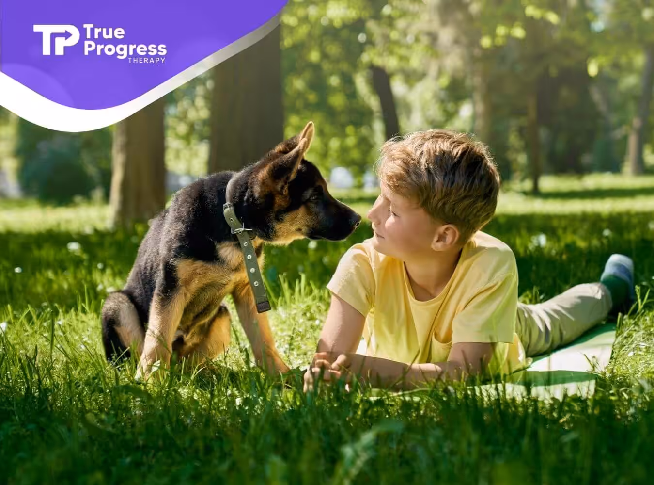 Autistic boy lying on grass with a service dog.