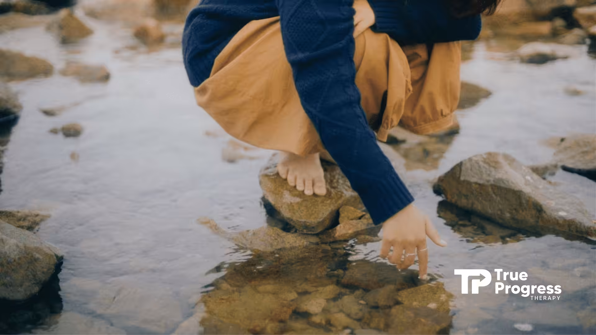 A person with autism crouching near a rocky stream, gently touching the water in New Jersey.