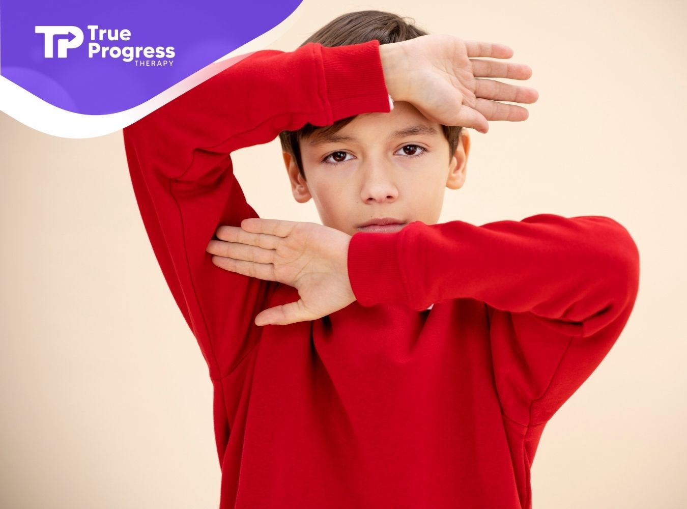 Autistic child in a red sweatshirt posing with hands framing their face.