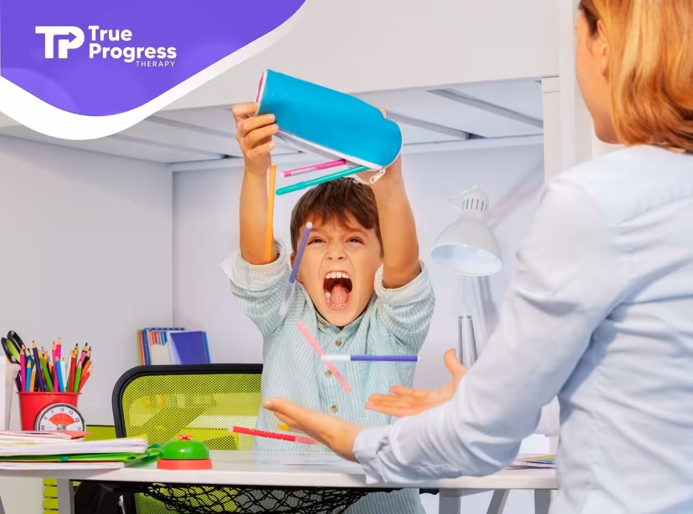 A young boy excitedly tosses colorful pens from a blue pencil case while sitting at a desk. An adult holds out hands to catch them.