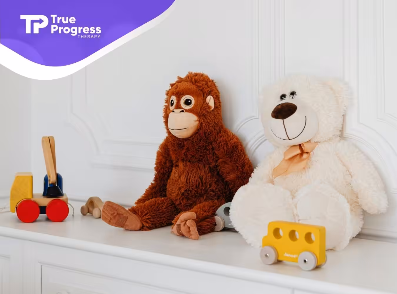 Brown monkey and white calming stuff toy sit on a shelf with wooden toys around them at home in NJ.