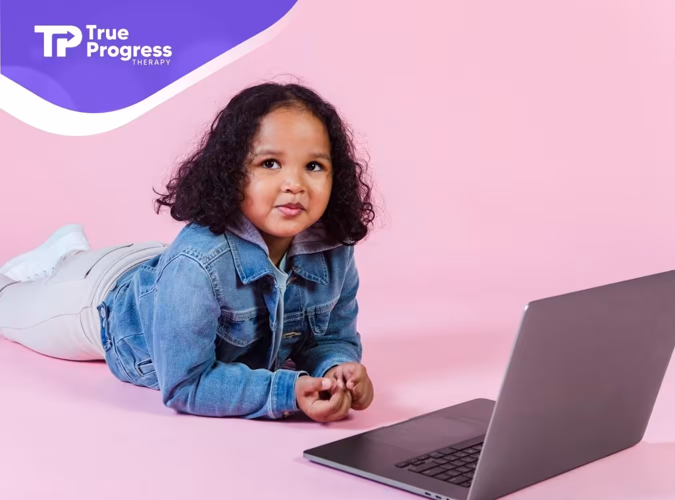 An autistic child lying on the floor in front of a laptop with a pink background during telehealth ABA session in NJ.