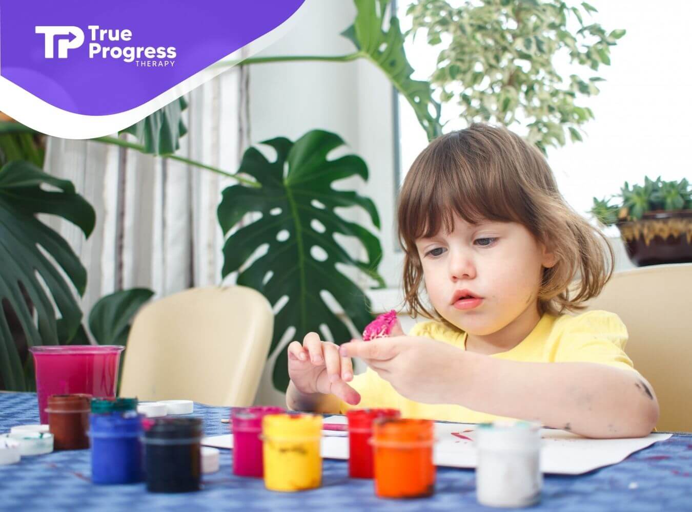 Young child painting at a table with colorful paint jars during ABA therapy.