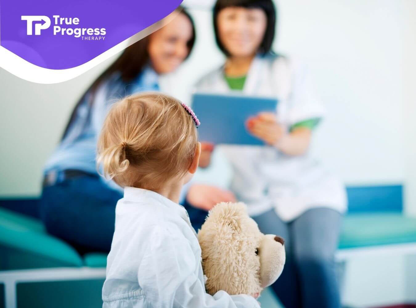 A young autistic child holding a teddy bear while two clinicians review a clipboard during a developmental therapy session.