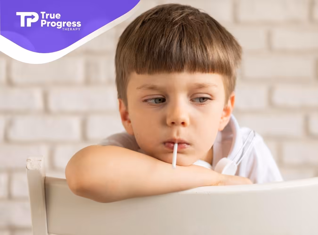 A young boy sitting and looking contemplative while holding a lollipop.