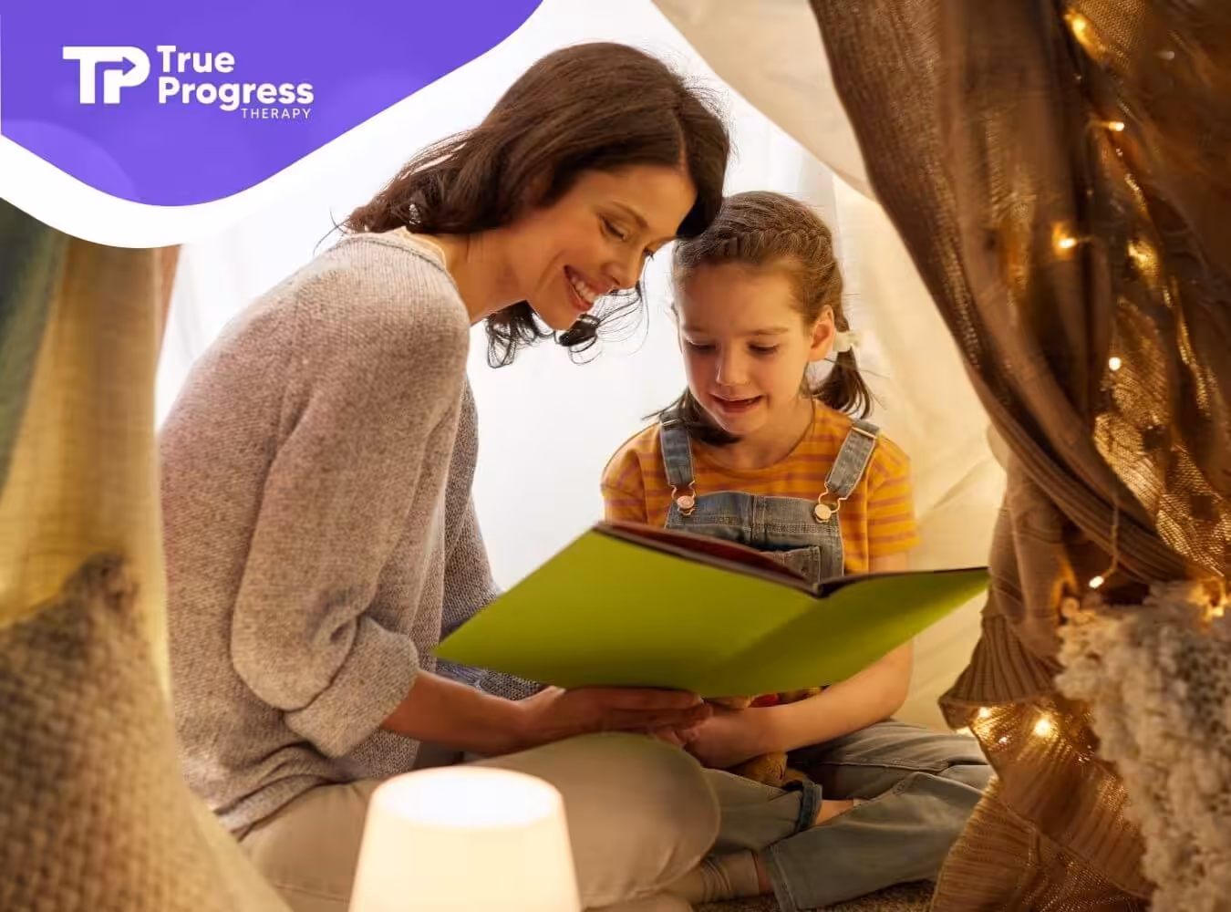 Female BCBA and autistic girl reading in a blanket fort in ABA therapy.