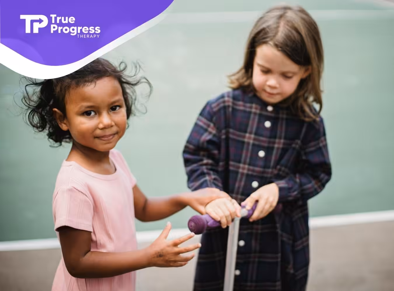 Two autistic girls holding a scooter, one smiling at the camera during center-based ABA therapy in New Jersey.