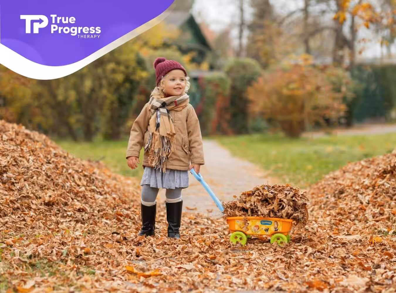 Bundled-up child in fall outfit pulls yellow toy wagon filled with dry leaves along a leafy autumn path.