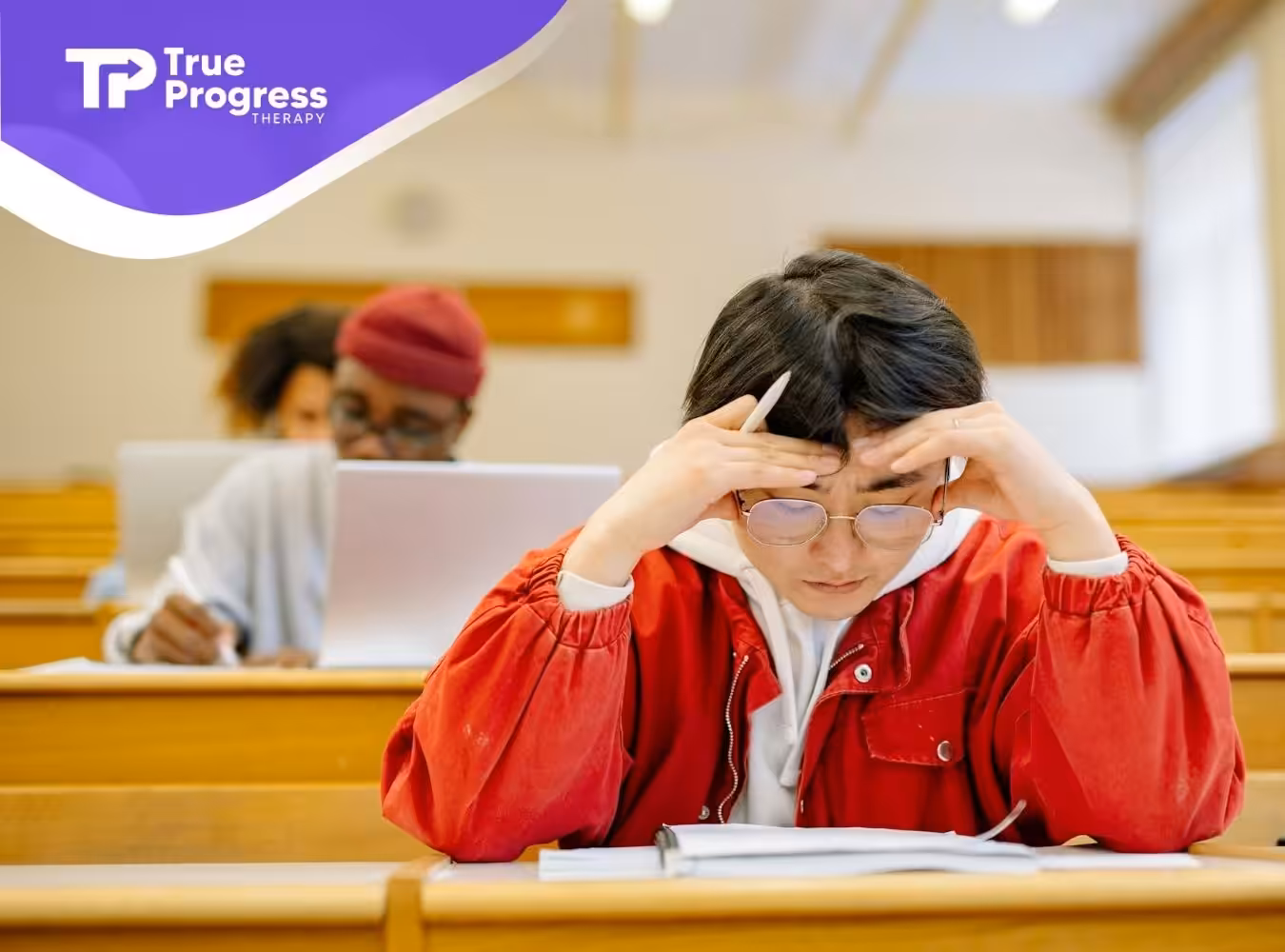 A stressed BCBA student in a red jacket taking his first BCBA exam at a lecture hall in New Jersey