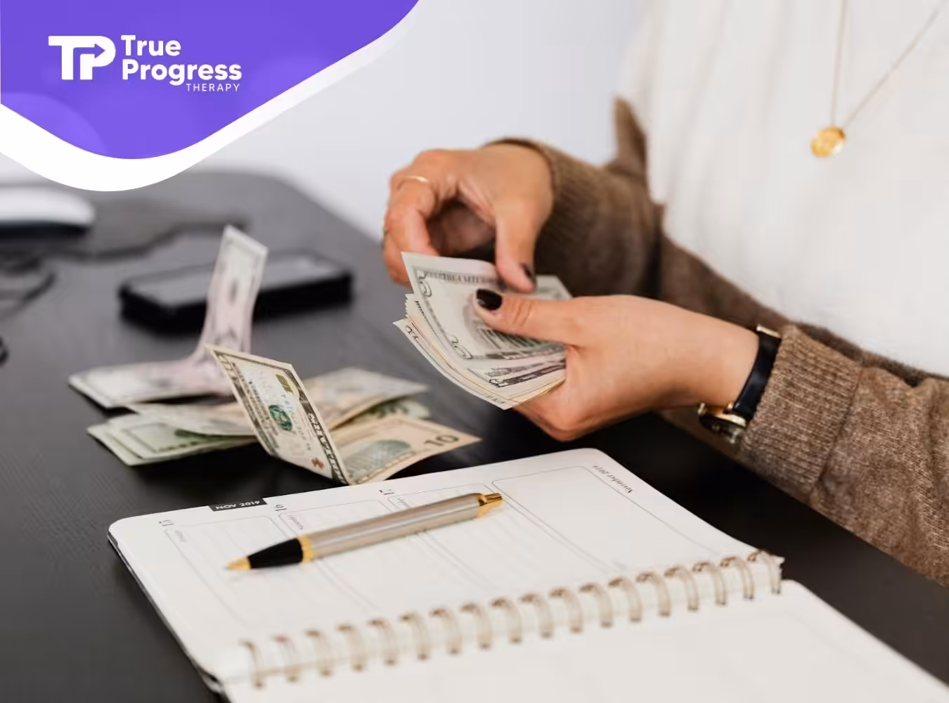 Caregiver of an autistic child counting US dollar bills beside a notebook and pen on a desk for ABA therapy expenses.
