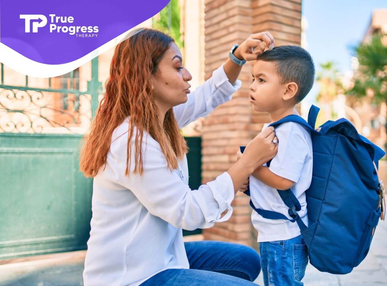 BCBA adjusting autistic child's backpack outside a school gate.