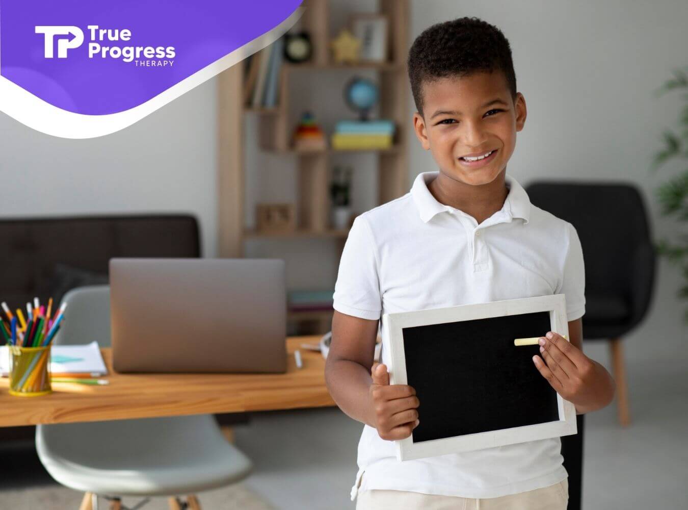 Smiling school-aged autistic boy holding a chalkboard in a home learning space, representing confidence and academic progress