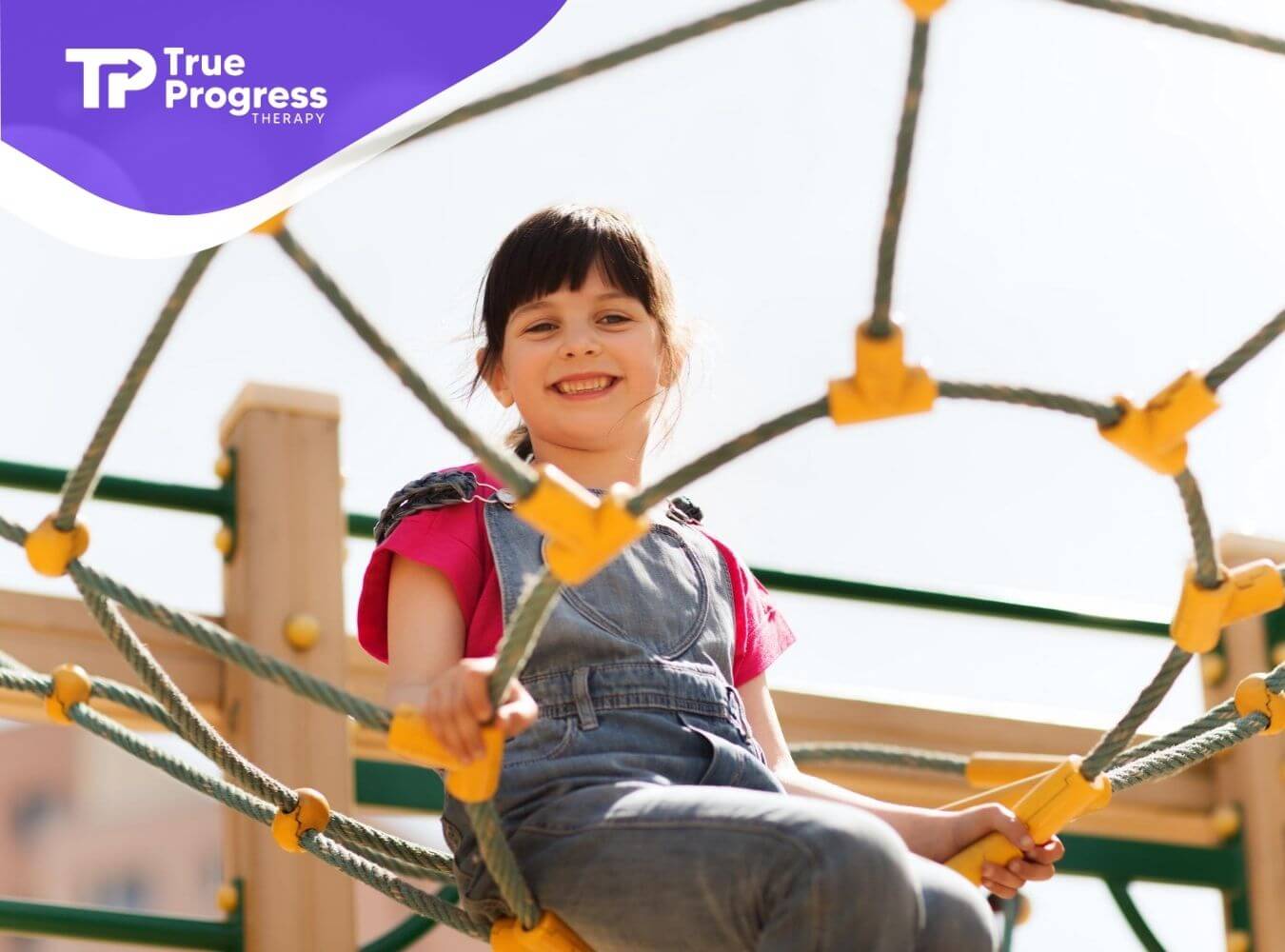 A smiling girl with autism climbing on a rope structure at a playground in NJ.