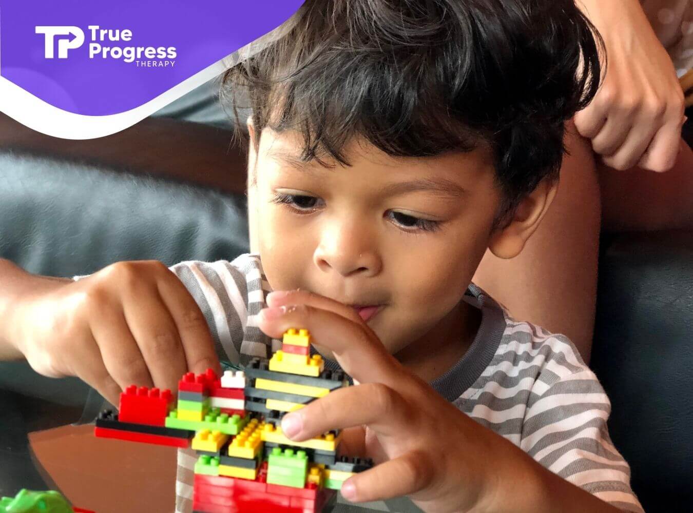Young autistic kid concentrating while building with colorful blocks, demonstrating fine motor skills & focused play at home
