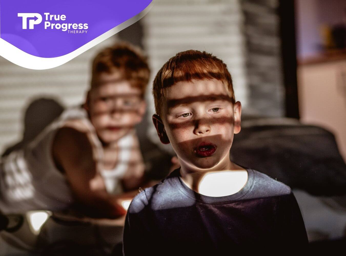 Two young autistic children indoors with sunlight shadows across their faces, showing quiet focus and emotional awareness.