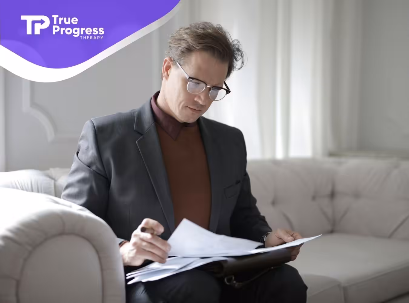 A professional BCBA in glasses reading documents on a sofa, preparing ABA treatment plans for autistic patient in NJ.