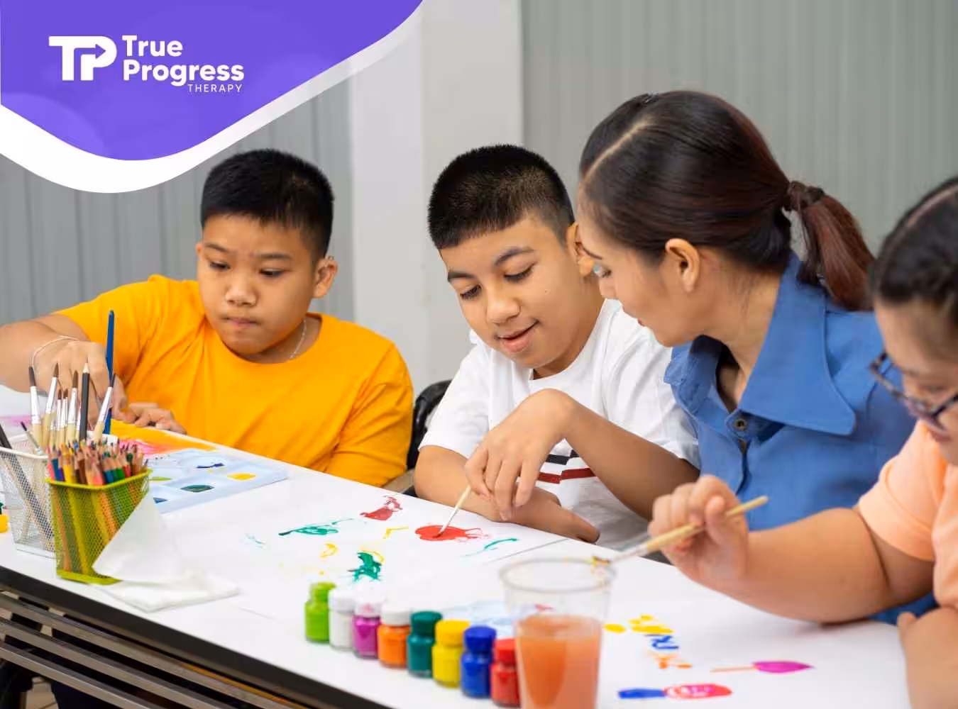 A group of children and an adult engage in a cheerful painting activity. They're focused on colorful artwork with paints, pencils, and brushes on the table.