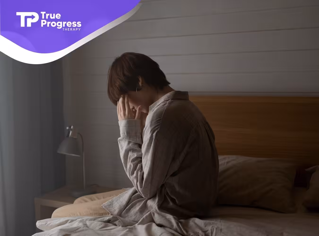 A person sitting on a bed, looking distressed, in a softly lit bedroom.