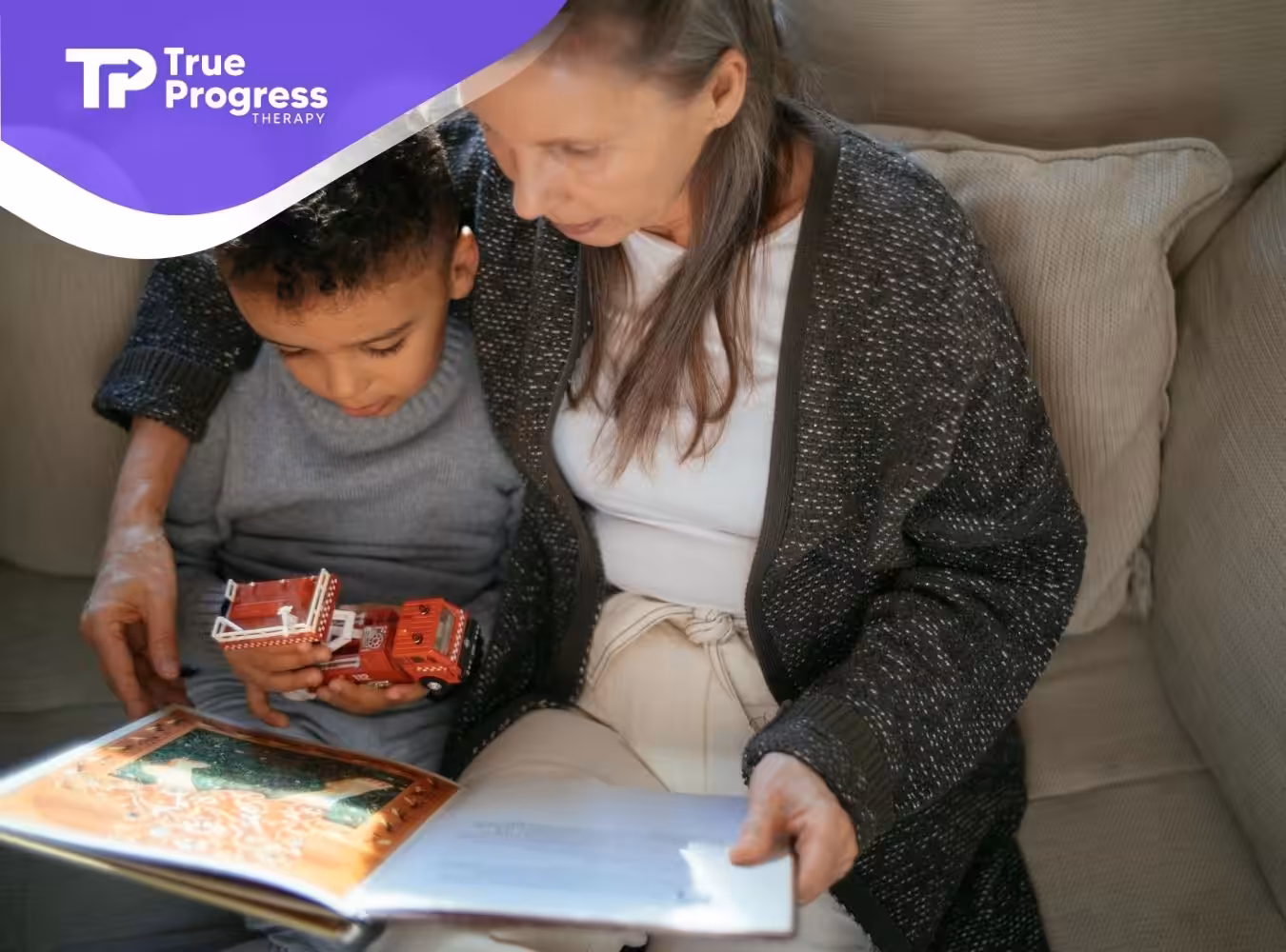 An ABA therapist and autistic child are reading a book, while he holds a red toy fire truck in NJ.
