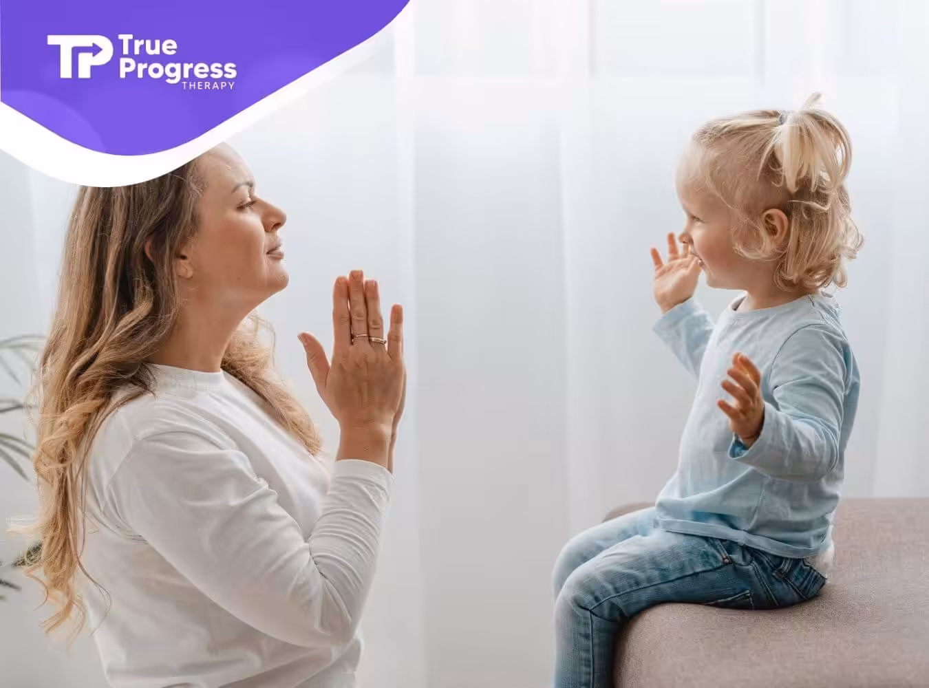 A BCBA and toddler with autism smiling and playing together while facing each other in a bright room.