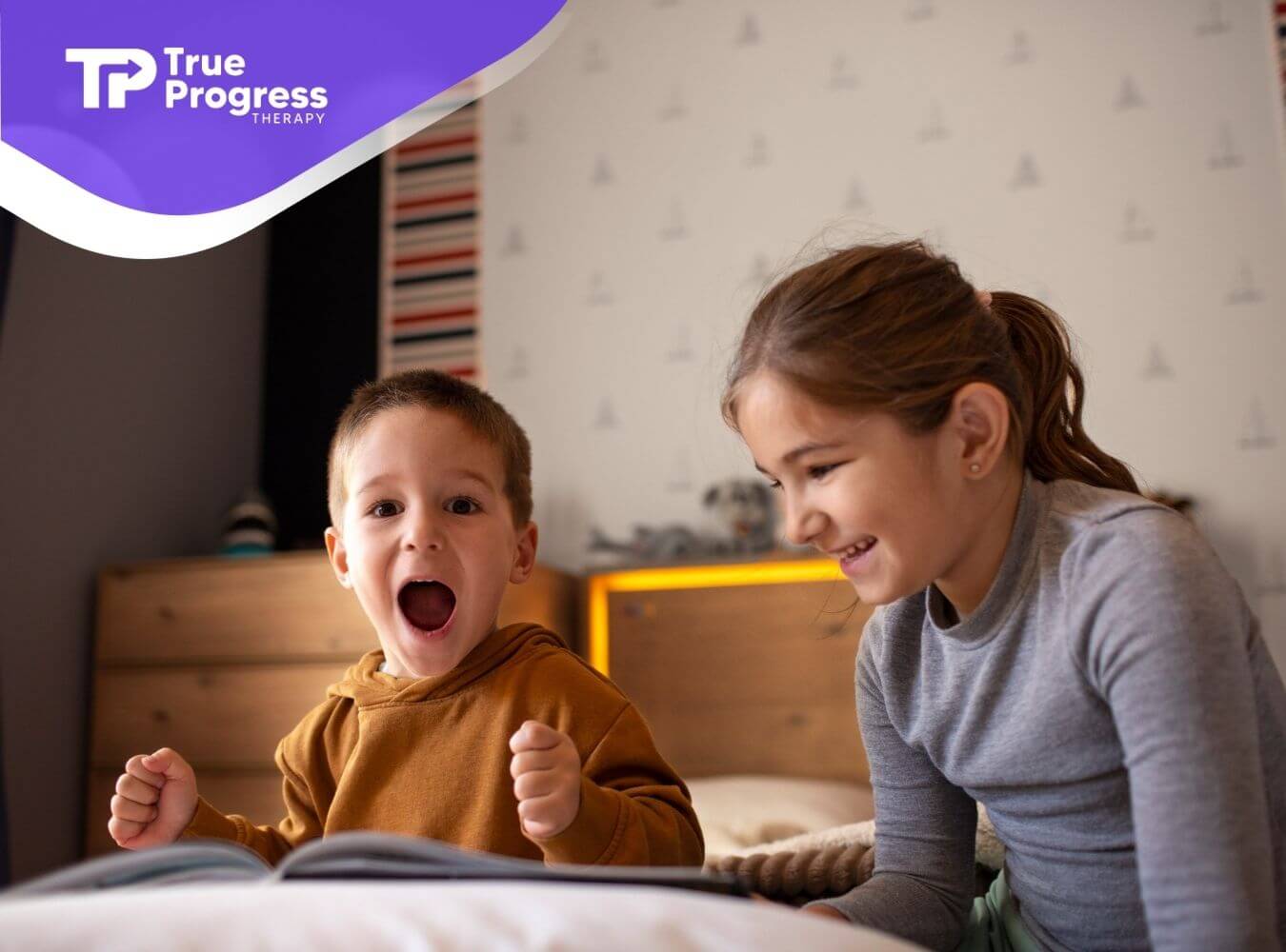 Young boy with autism cheering excitedly while an older girl smiles beside him during a a group ABA therapy session.