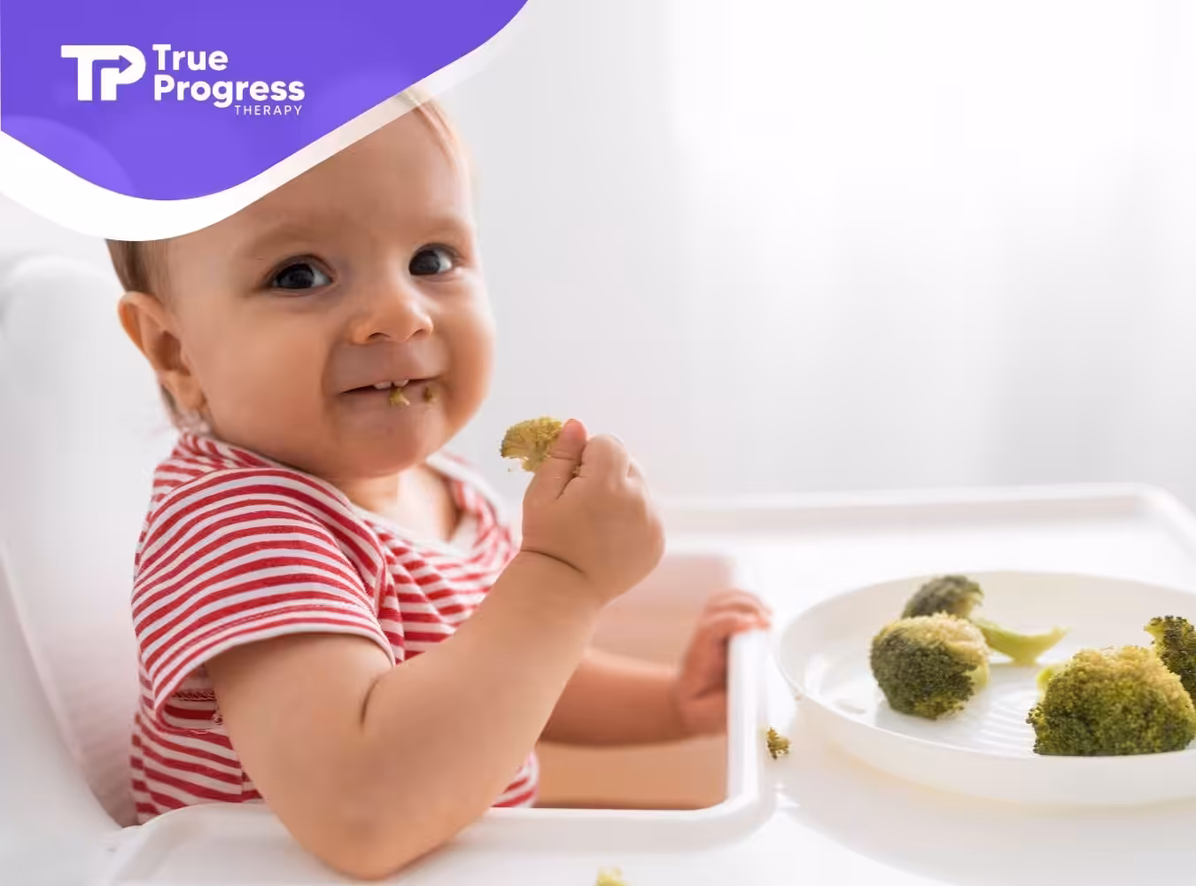 A toddler eating broccoli while sitting in a high chair.