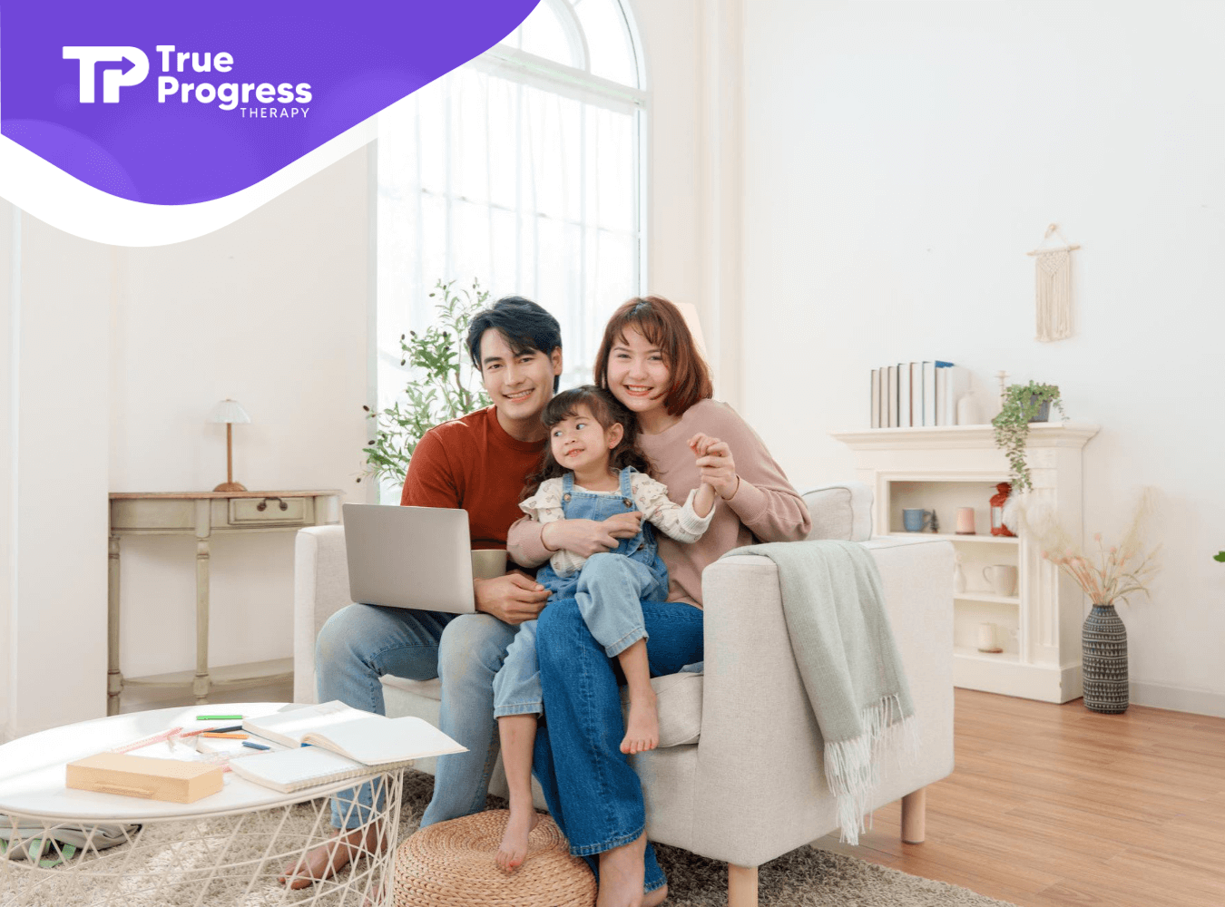 Parents sitting on a couch with their young child and a laptop in a bright living room.