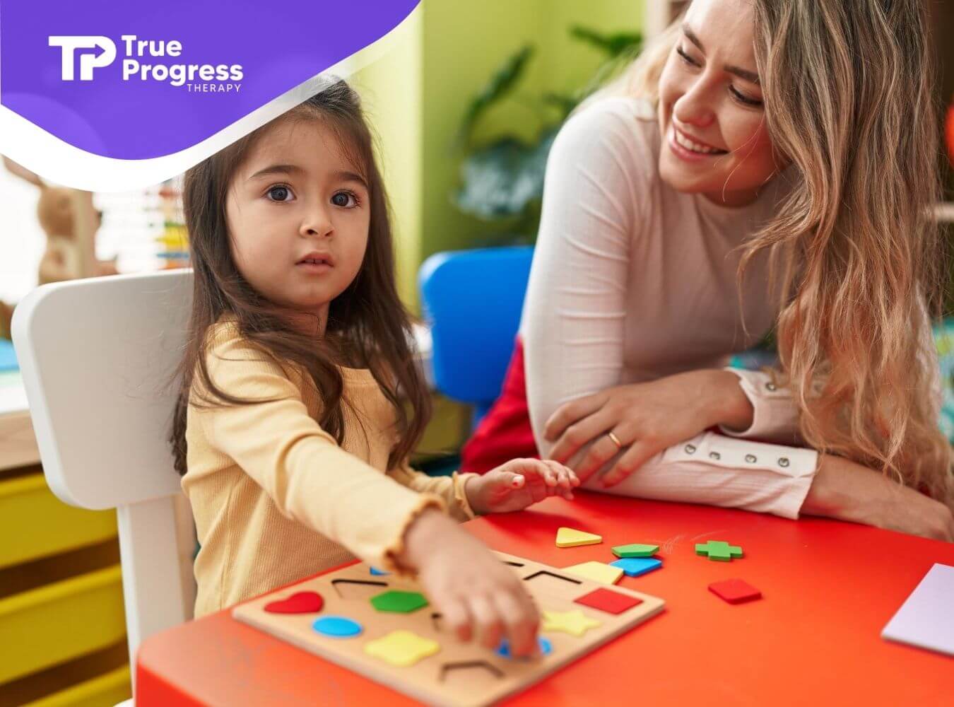 Young child doing a shape puzzle with an ABA therapist nearby.