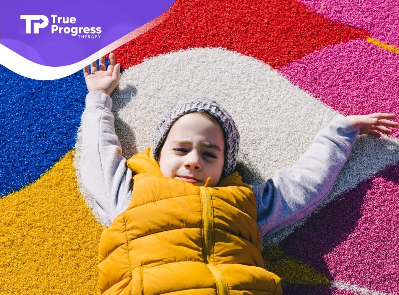 Child with autism lying on a colorful playground surface with arms stretched out.