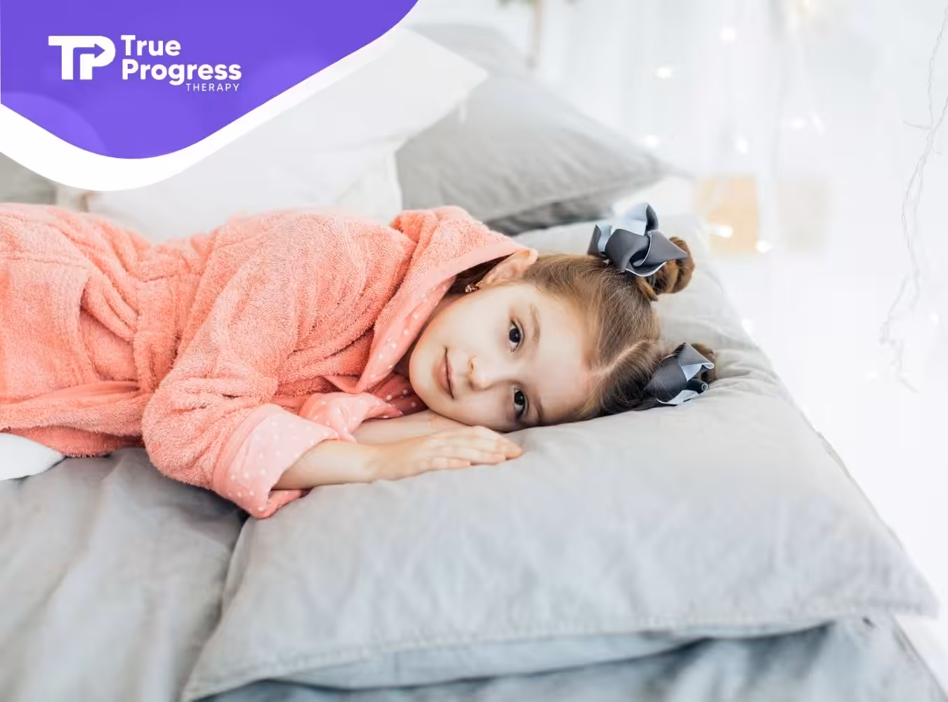 An autistic girl in pink robe lying and resting on pillows while looking at the camera after ABA therapy in NJ.