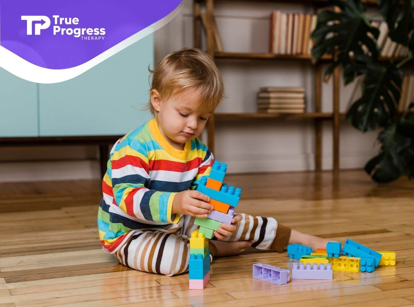 Toddler with autism sitting on the floor stacking colorful building blocks during ABA therapy.