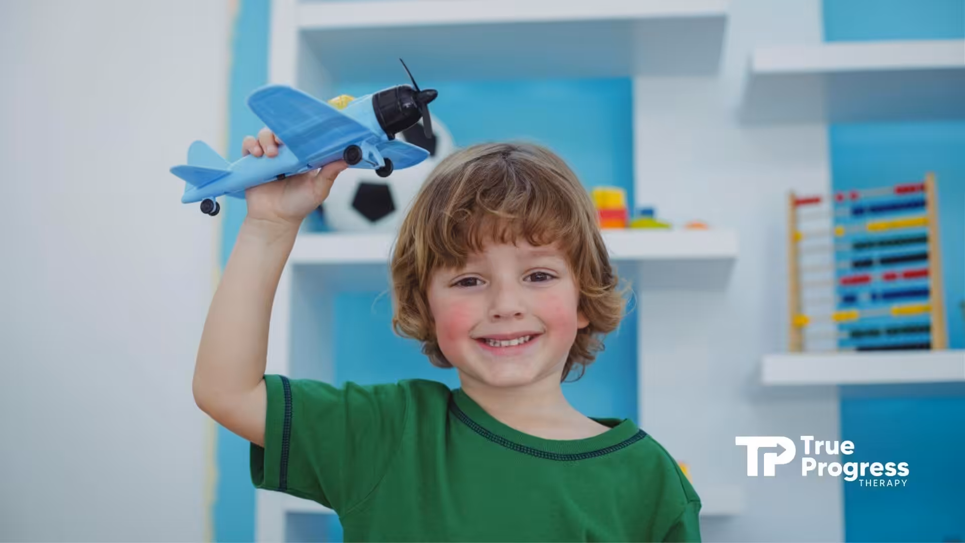 Autistic boy smiling with a blue toy airplane in ABA therapy.