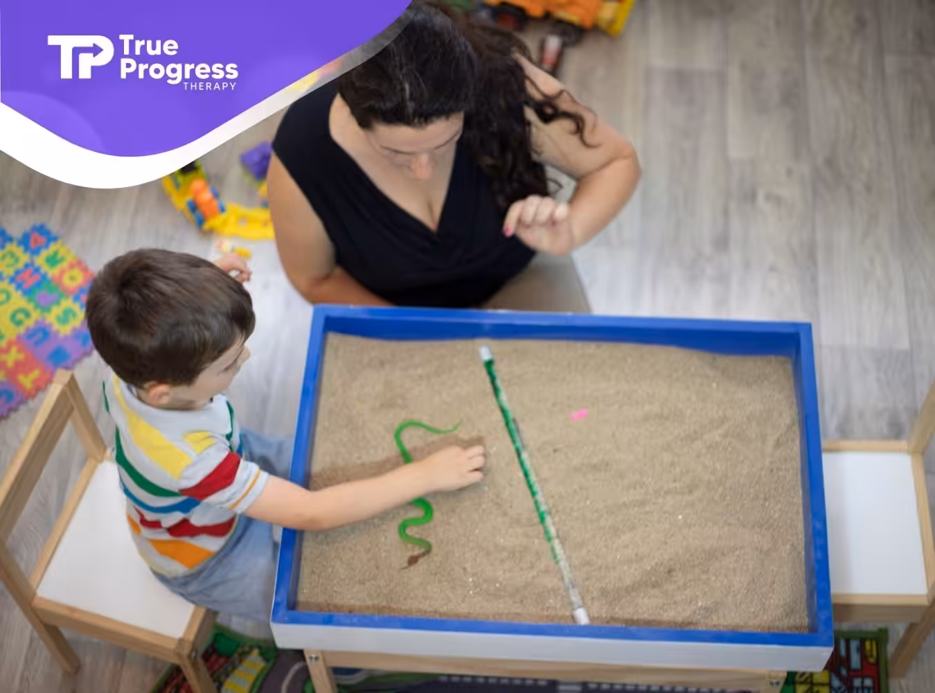 A little boy playing with sandbox with his ABA therapist.