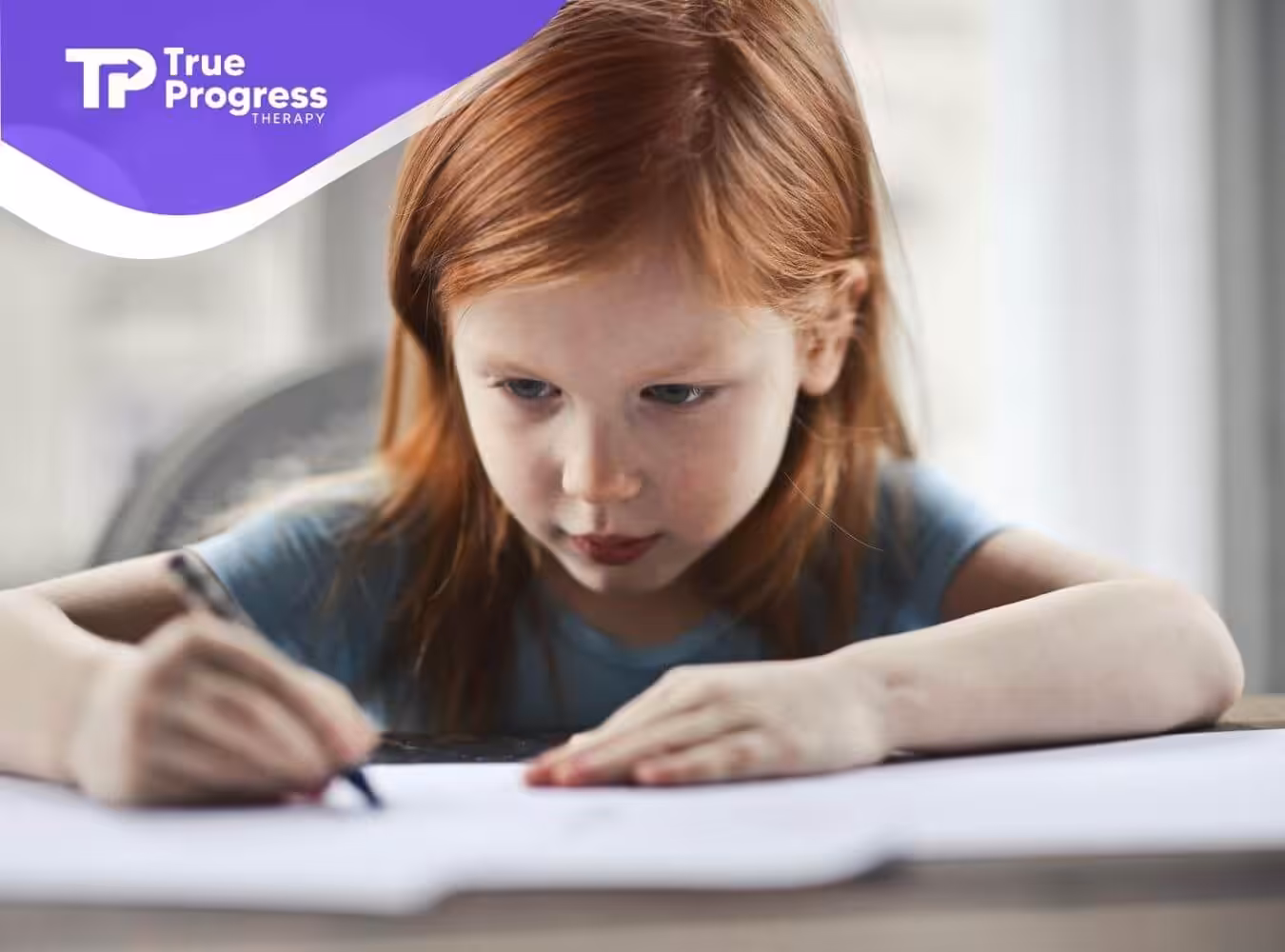 Red-haired child in blue shirt focuses on drawing with pencil at a sunlit table near a softly lit window.