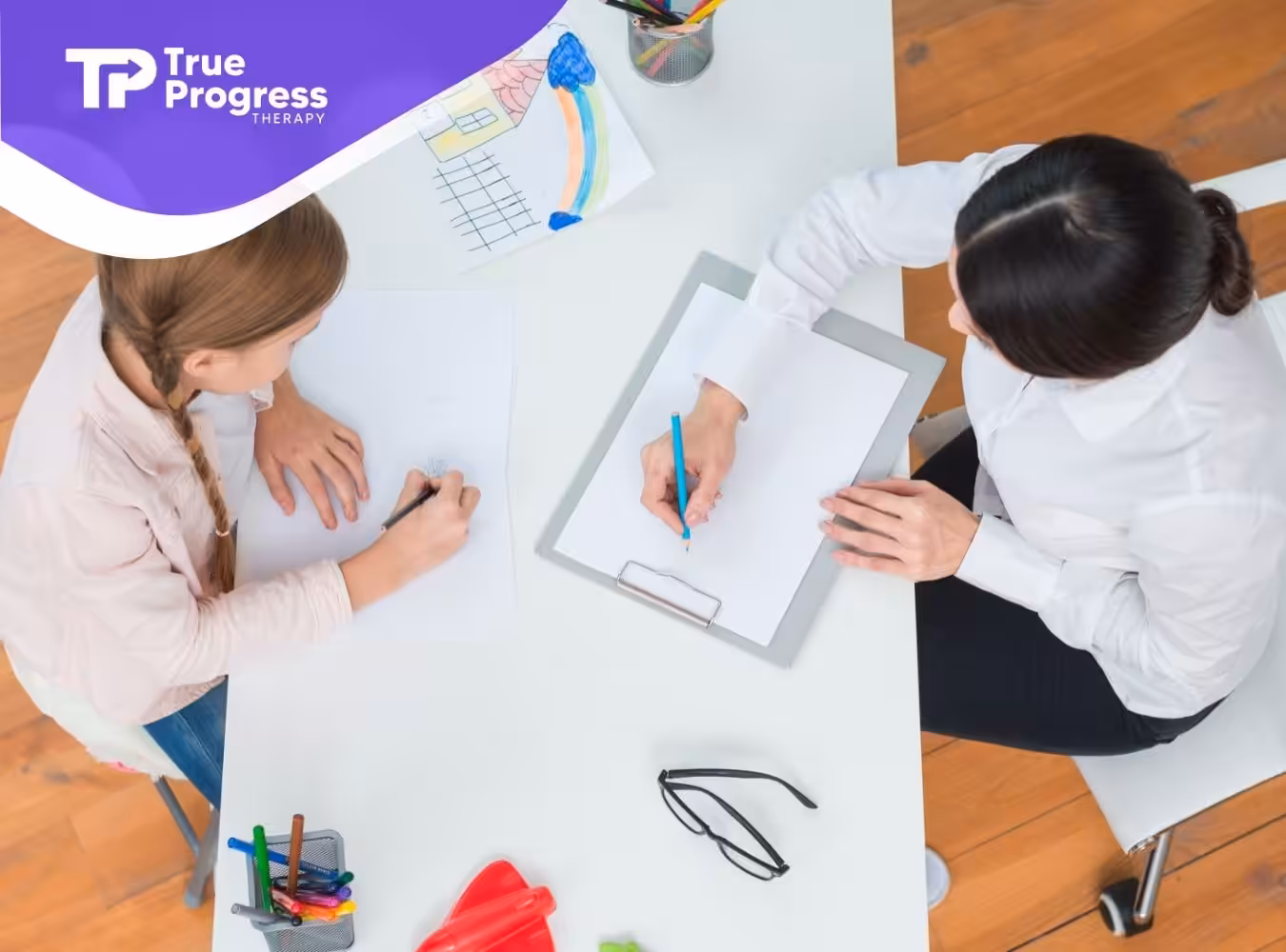 Top-down view of a child and an ABA therapist working together on drawings and notes.