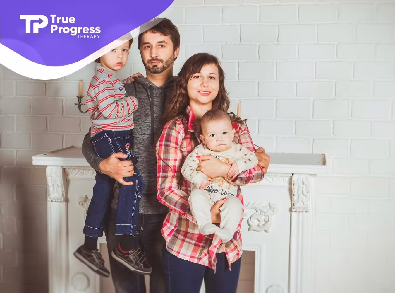 A family of four posing in front of brick wall in NJ, with parents holding their autistic children.