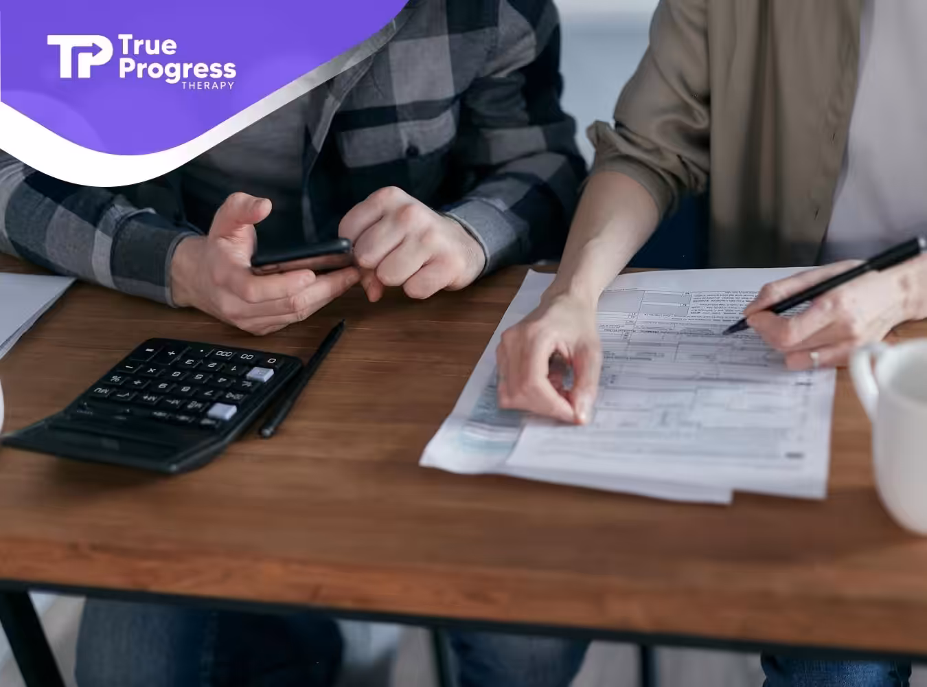 Two ABA therapists reviewing insurance documents for ABA therapy with a calculator and coffee mug on the table.