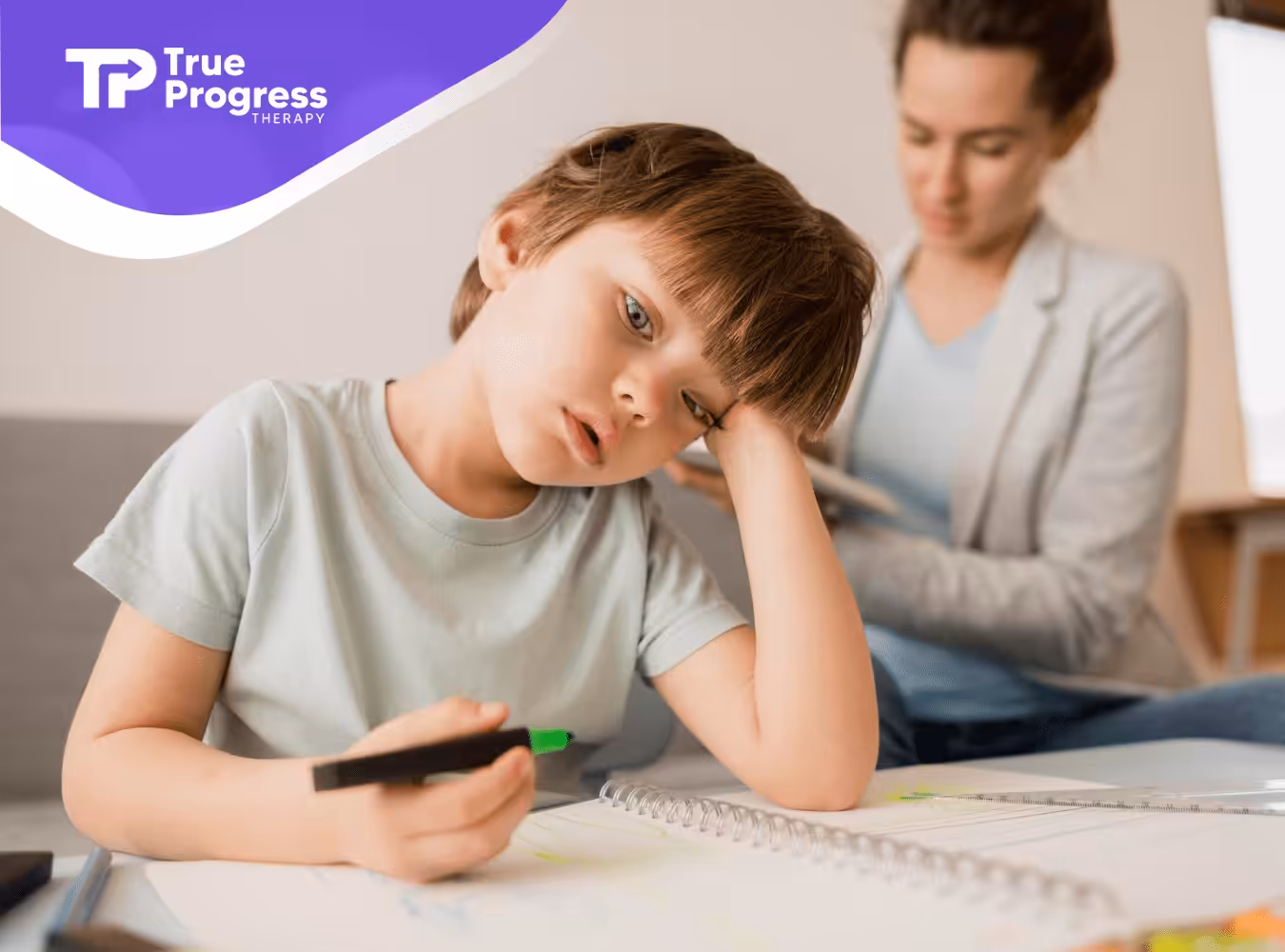 A boy with autismholds a marker and looks tired while drawing at a table.