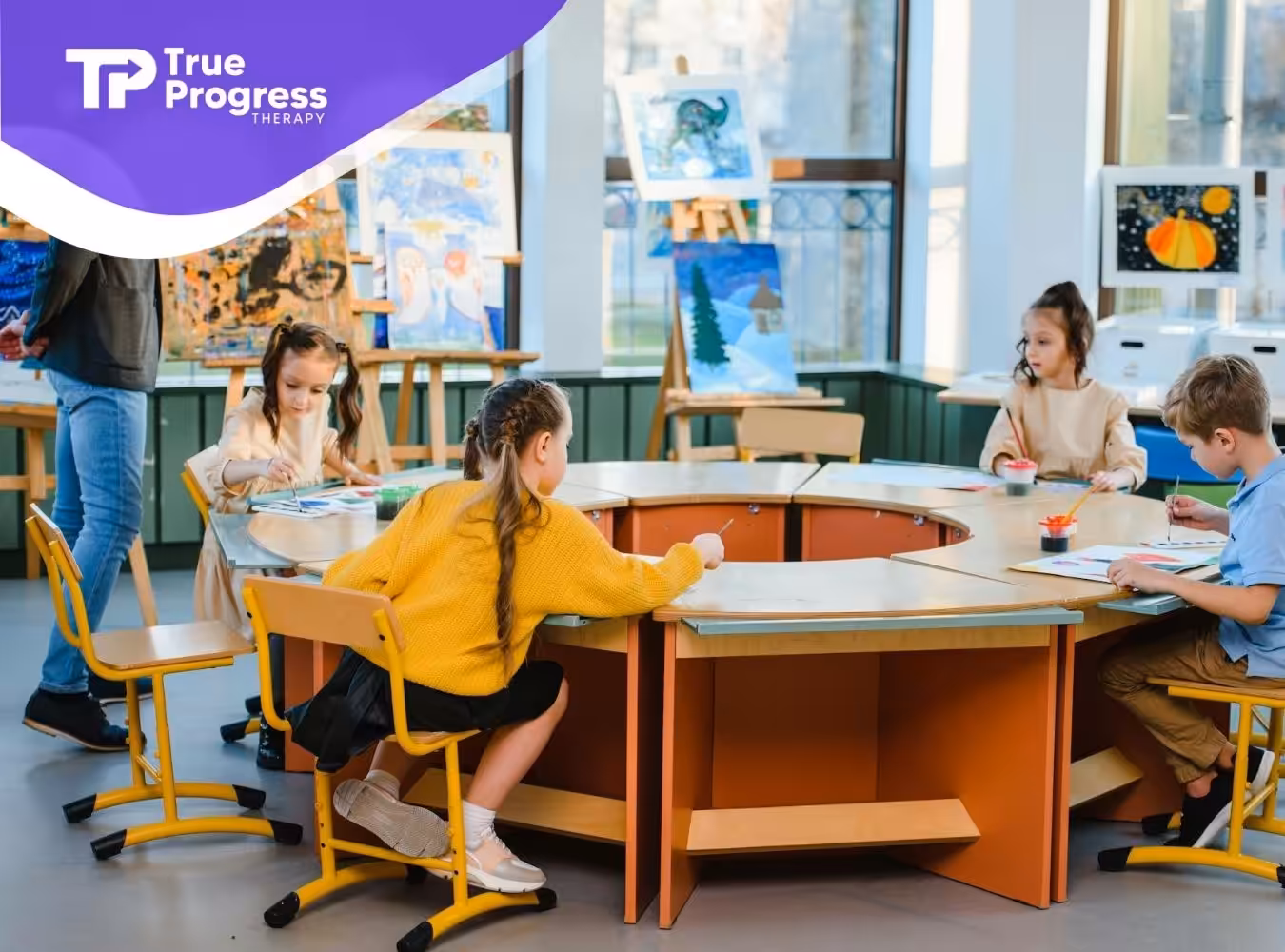 Autistic children seated around a table, painting in a classroom with a behavioral therapist in NJ.