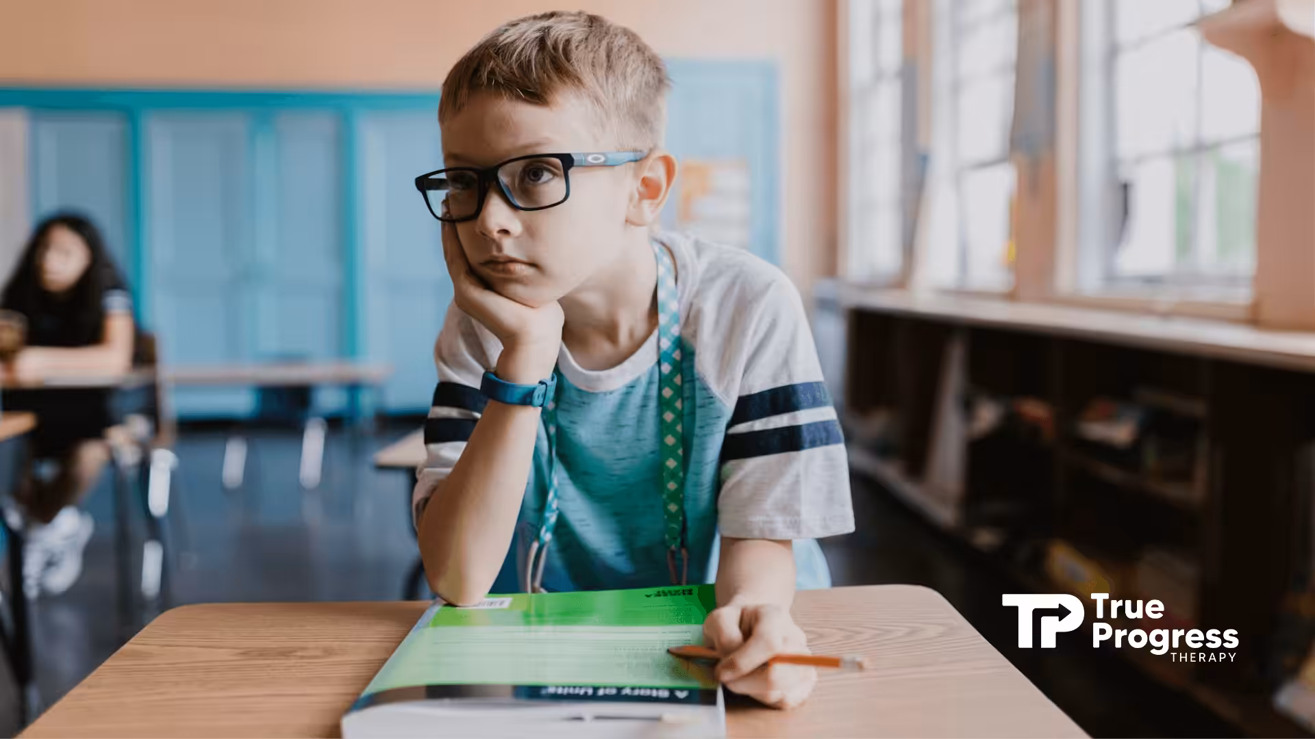 An autistic boy in glasses leaning on hand at school desk, looking thoughtful during school-based ABA therapy in NJ.