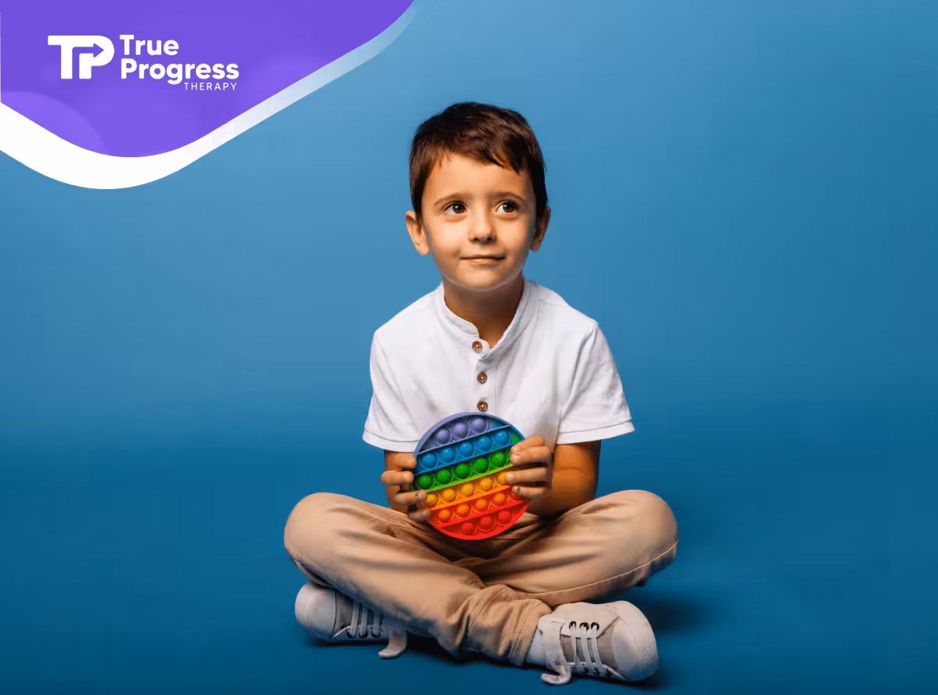 A child with autism is sitting on the floor holding a colorful fidget toy