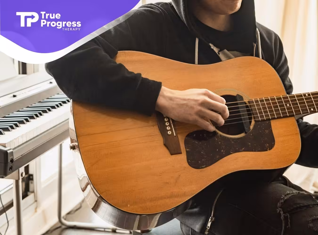 Ed Sheeran, a famous singer suspected of autism, wearing hoodie playing acoustic guitar near keyboard.